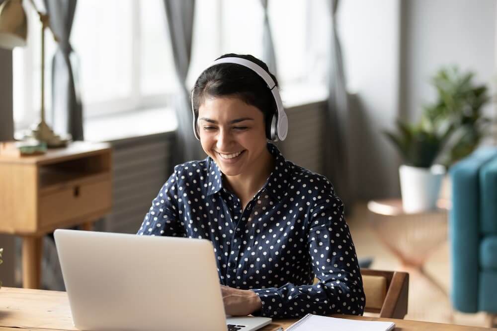 Young adult woman smiling in front of laptop while wearing headphones