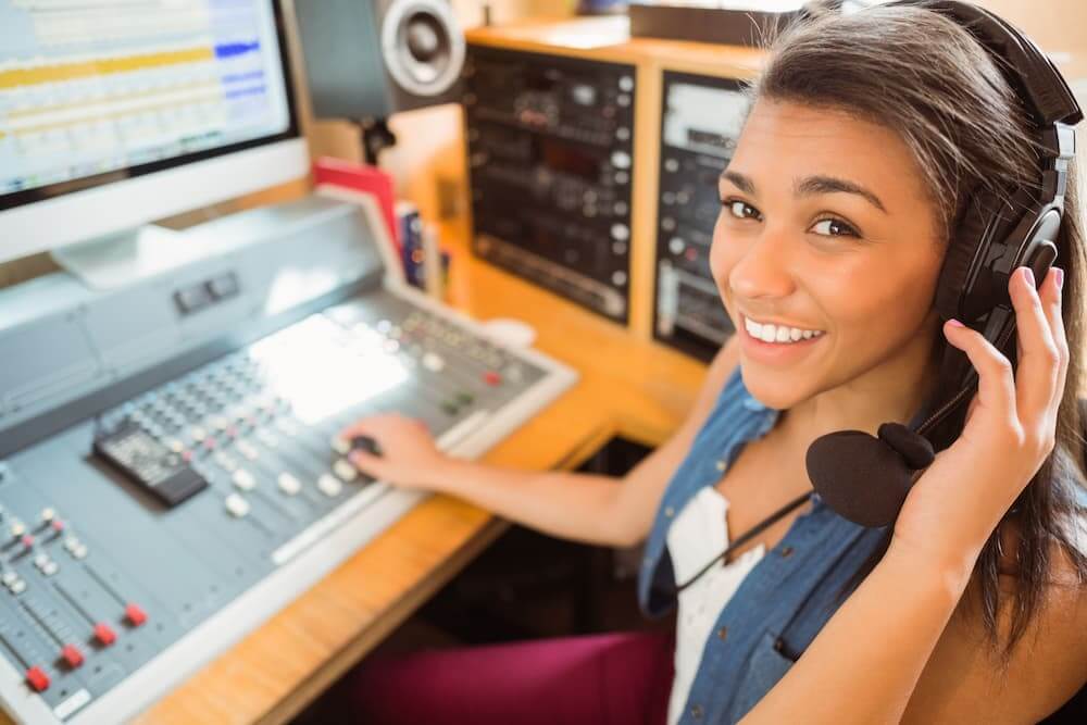 Girl smiling while wearing a headset and sitting in front of broadcasting equipment