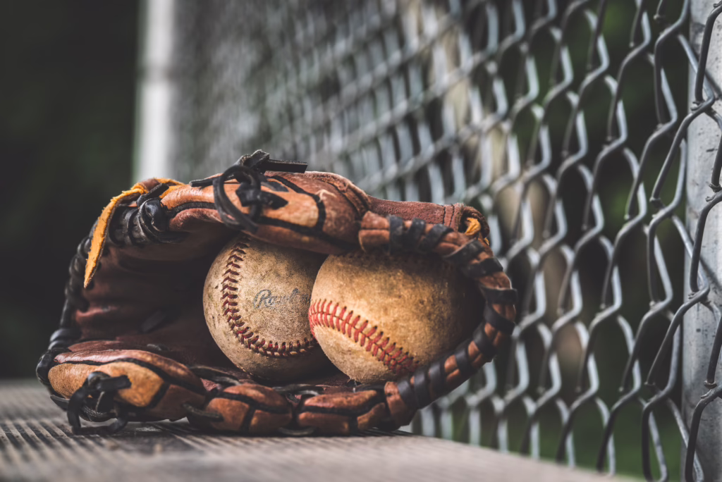 Two worn baseballs resting in a leather glove beside a chain-link backstop