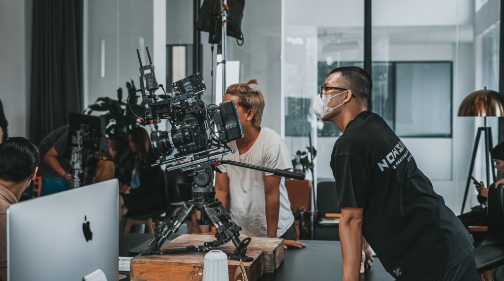 Crew members checking a cinema camera on a tripod during setup before the camera rolls on an indoor set
